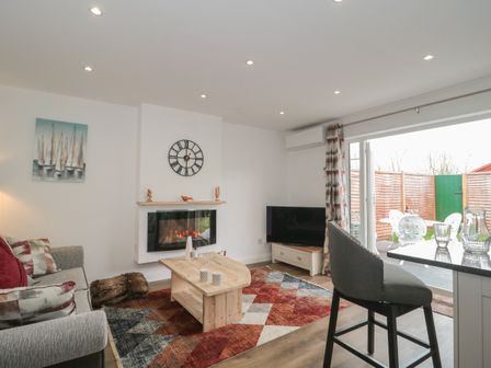 A living room with a sofa coffee table fireplace TV and open doors leading to a garden at The Hideaway in Lympsham near Brean