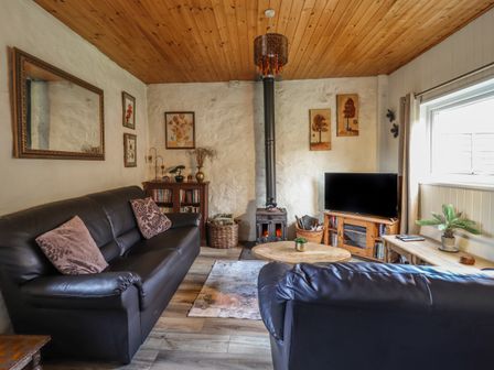 A living room with two black sofas a wood stove a television on a stand and wall art at Tyn Y Cefn Near Blaenau Ffestiniog