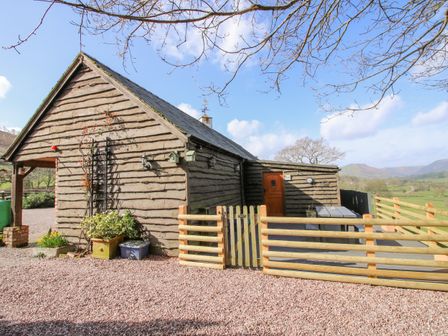 A wooden cottage with a fenced gravel area and mountains in the background at The Retreat in Pedairffordd near Llanrhaeadr-Ym-Mochnant