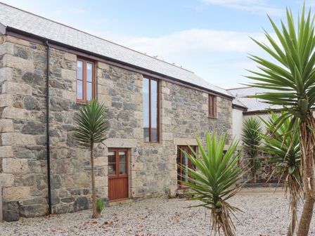 Exterior view of a stone building with multiple windows and doors surrounded by gravel and tall spiky plants at Pol Glas Hall in Cury near Mullion