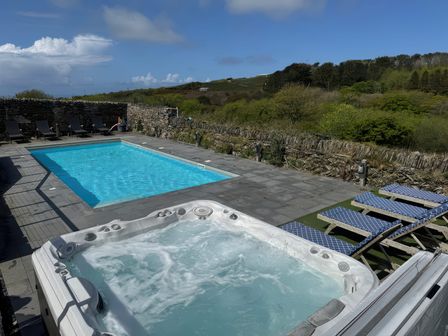 An outdoor area with a swimming pool hot tub and lounge chairs surrounded by stone walls and greenery at Penpethy Farm in Tintagel
