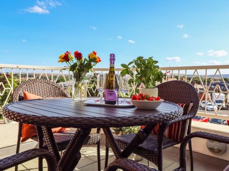 A balcony with a round wicker table and chairs with a bottle of prosecco glasses flowers a plant and strawberries at Above & Beyond Whitby