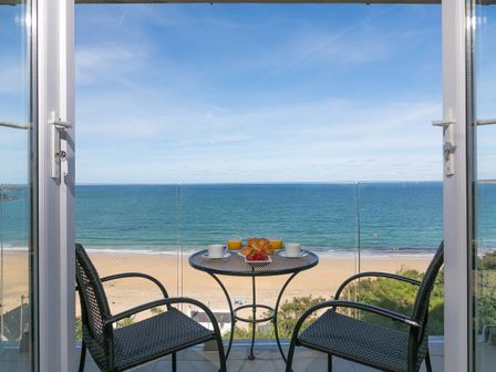 A balcony with a small table and two chairs overlooking a beach and ocean at Ivory in Carbis Bay