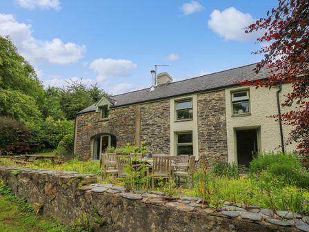 A stone cottage with outdoor wooden dining furniture and garden surrounded by greenery at Taibach in Dinas Cross