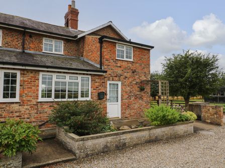 A brick house with white framed windows and a white door with plants in a raised garden bed at 2 Crosslands in Stockton-On-The-Forest