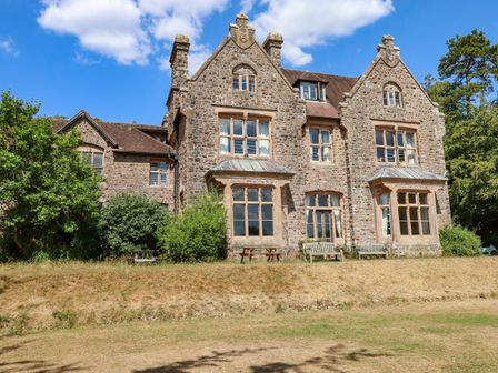 An exterior view of a large stone building with multiple windows and wooden benches outside Nethercott House in Iddesleigh near Hatherleigh