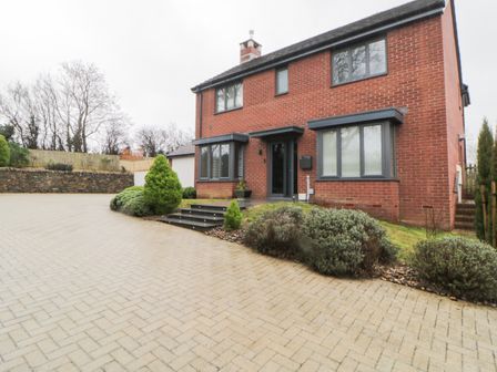 A brick house with black framed windows and a driveway with shrubs and trees at 2 White Rock Court in Paignton