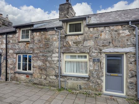 Stone exterior wall with three windows and a gray door on a paved sidewalk at Cuddfan in Tremadog