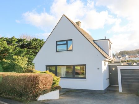 A white house with a triangular roof and two windows with a driveway and greenery at 8 Little Hill in Salcombe