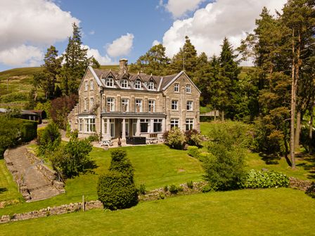 A large stone house with a lawn and trees around it at Heatherbrae in Middleton-In-Teesdale