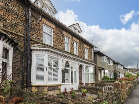 A stone building with white windows and a small garden in front on a residential street at Beckmead in Windermere