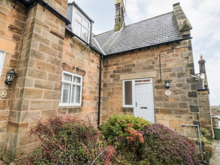 The exterior corner of a stone house with a white door and window surrounded by bushes at 4 Maypole Green in Fylingthorpe