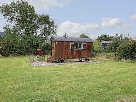 A wooden shepherds hut on wheels with outdoor chairs and a table on a grassy area at Brown Hare Shepherds Hut in Llangorse