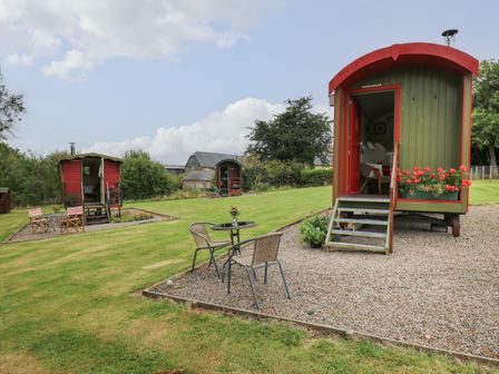 A grassy outdoor area with three small green and red shepherds huts and outdoor seating at Sweet Briar Shepherds Hut in Llangorse