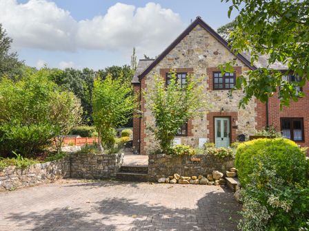 A stone and brick house with a green door surrounded by trees and shrubs at Barley Cottage in Weycroft near Axminster