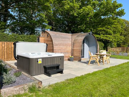 A wooden pod structure with a hot tub patio and table with two chairs on grass at Yr Onnen in Bontuchel near Ruthin