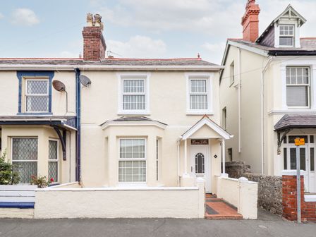 The front view of a terraced house with cream walls and white window frames at Owen Villa in Llandudno