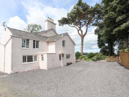 The exterior of a two story house with multiple windows a gravel driveway and trees in the background at Frongoch Cottage in Red Wharf Bay near Pentraeth
