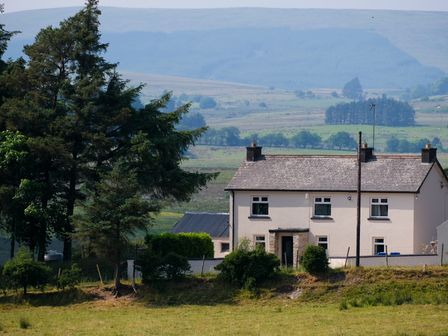A farmhouse with trees around and hills in the background at Peters Farmhouse in Cookstown