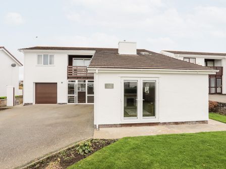 A white two-story house with a garage driveway and a lawn at Llwyn Eithin Trearddur Bay
