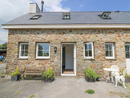 A stone house facade with three front windows an open door two potted plants a bench and a white metal table with chairs at The Old Stable in Bettws