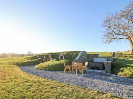 An outdoor grassy earth shelter with round windows a wooden table with four chairs and a hot tub at Tan y Wawr- Onnen in Llanfair Caereinion