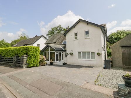 A white two-story house with a tiled driveway and hedge next to it at Holme Fell in Coniston