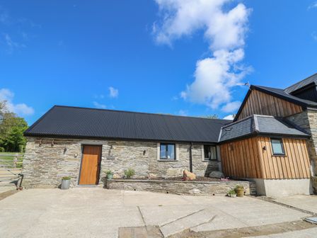 A stone and wood house with a black roof and a small garden bed at The Parlour in Llangoedmor near Cardigan