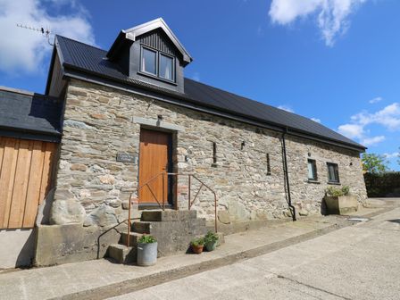 A stone cottage with a wooden door and small steps with flower pots at Cattle Tree Cottage in Llangoedmor near Cardigan