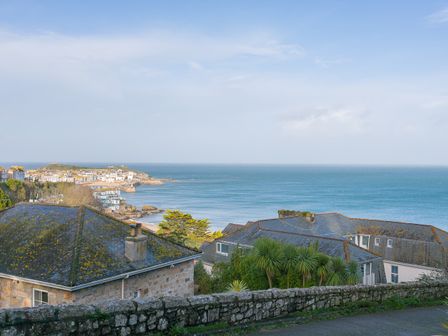 A coastal view with houses, a stone wall, vegetation, and the sea in the background at St Ives View in St Ives