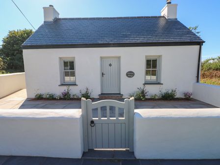 A white cottage with a grey roof and gate with flowers along the front at Catamouse in Milford Haven