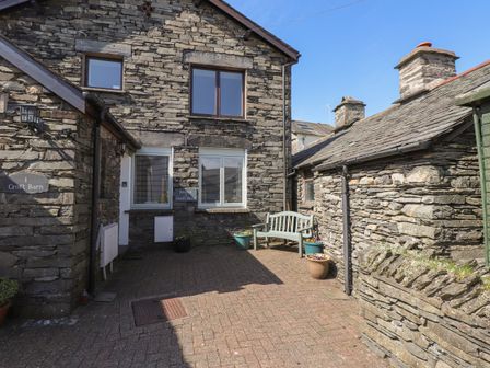 An outdoor courtyard area with stone walls a bench flower pots and two doors at Jenny's Croft Barn in Hawkshead