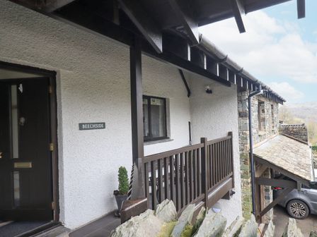 An exterior view of a building entrance with a balcony railing and a parked car at Beechside in Ambleside