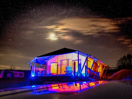 A tent lodge lit with colorful lights under a starry sky with the moon and clouds at Semira Tent Lodge in Blackawton