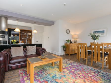 An open living and dining area with leather sofas wooden tables and chairs and a colorful rug at Arghanti in St Ives