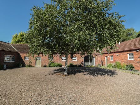 A courtyard with a tree in the center surrounded by brick buildings at Cheviot View in Crookham near Cornhill-On-Tweed
