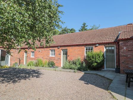 A red brick building with green doors and windows in a garden area with gravel and plants at Flodden in Crookham near Cornhill-On-Tweed