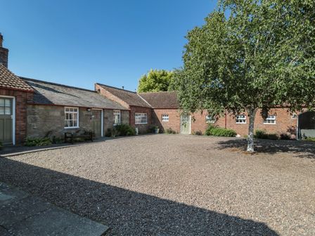 A courtyard with gravel ground a tree and stone and brick buildings at Bakers Cottage Crookham near Cornhill-On-Tweed
