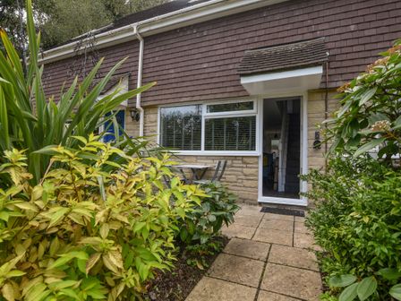 A small stone patio with plants and a table outside the front door of a house at 51 Fernhill Heights in Charmouth