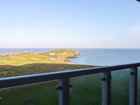 A coastal view with a grassy headland and ocean behind a glass balcony at 9 Headland Point in Newquay