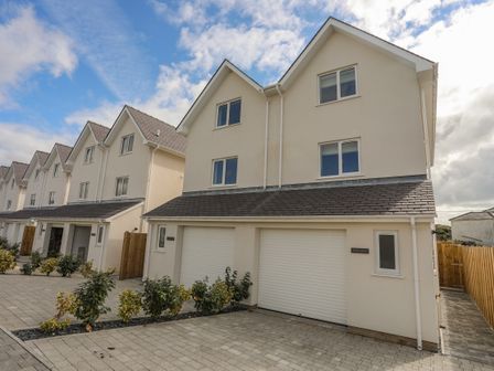 A row of attached houses with garages and small bushes in front at 9 Lon Y Dryw in Trearddur Bay