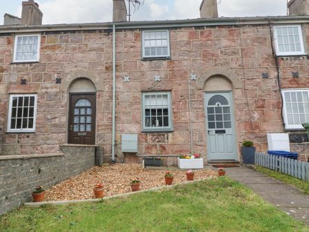 Stone terraced houses with two doors and four windows with flower pots in front at Llety Bach in Caernarfon