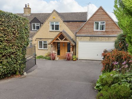 A driveway leading to a house with wooden front door and garage surrounded by plants and greenery at The Gables in Sheepscombe