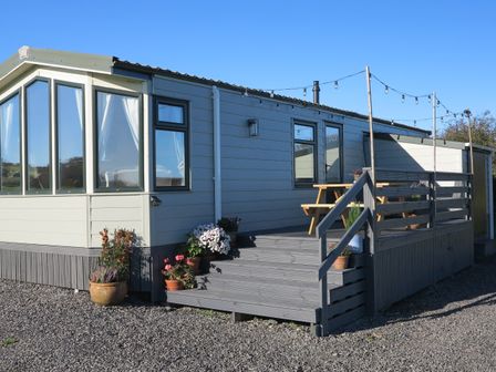 A caravan with a wooden deck and potted plants outside at Plas Tirion Caravan in Llanfairynghornwy near Cemaes Bay