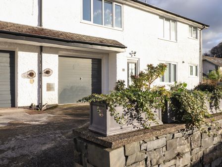 The exterior of a white building with large windows grey garage doors and planters with greenery on a stone wall at Tipsy Bee in Bowness-On-Windermere