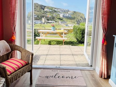A living room with a view of a grassy area and outdoor table at Kippy Cottage in Truro