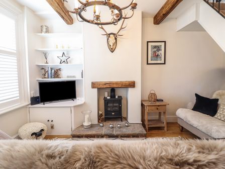 A living room with a wood stove under a wooden beam and shelves with a television at Glynside in Conwy