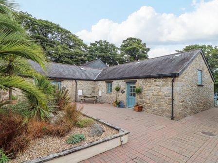 Stone cottage with blue door and windows with a paved courtyard and plants in a garden bed at Budock in Mawnan Smith Near Falmouth