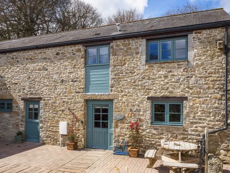 Stone exterior of a house with blue doors and windows and a wooden picnic table on a paved area at Kerensa in Mawnan Smith Near Falmouth