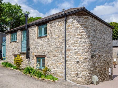 An exterior view of a stone building with multiple blue windows and plants along the base at Newlyn in Mawnan Smith Near Falmouth